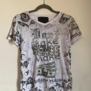 Vit t-shirt med tryck från Philipp Plein - Säljer en vit t-shirt från Philipp Plein med tryck av dödskallar och sedlar. Texten på framsidan lyder 'Don't Make Sense Make'. 