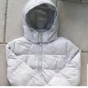 Grå gant dunjacka  - Säljer en stilren grå dunjacka med huva och dragkedja. Jackan har en quiltad design och en snygg rosa insida. Perfekt för kyliga dagar!