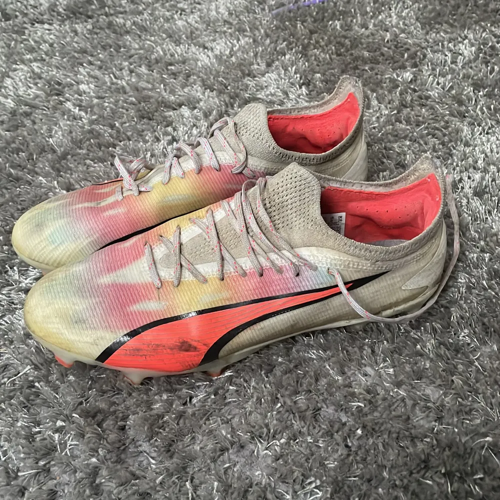 Säljer ett par färgglada fotbollsskor från Puma med snörning. Skorna har en mix av beige, rosa och gul färg med en svart detalj på sidan. Perfekta för fotbollsplanen!. Kengät.