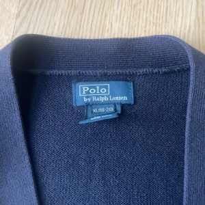 Mörkblå kofta från Polo Ralph Lauren - Säljer en stilren mörkblå kofta från Polo Ralph Lauren. Koftan har en v-ringad design med knappar framtill och två praktiska fickor. Perfekt skick utan defekter 