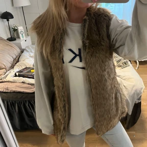 Brun pälsväst från Bershka - Säljer en snygg brun pälsväst från Bershka. Västen är perfekt för att lägga till lite stil och värme till din outfit. Den är ärmlös och har en mjuk, fluffig textur som ger en lyxig känsla. Passar bra över en tröja eller klänning.(inte äkta päls)