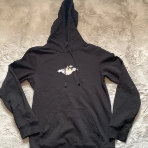 Svart hoodie från H&M - Säljer en svart hoodie från H&M i storlek XS. Tröjan har en justerbar huva med dragsko och en liten broderad detalj på bröstet. Perfekt för en avslappnad stil. Enda defekten är snörena som är lite sönder men går säkert att fixa.