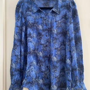 Blå mönstrad blus 44 - Säljer en blå mönstrad blus med långa ärmar och knappar framtill. Blusen har ett abstrakt mönster i olika nyanser av blått och svart. Perfekt för en stilren look. Ny marinblå och blå mönstrad genomskinlig blus i strl 44 från Inwear.  Ny, aldrig använd  Mått Över bröstet: ca 58 cm Längd från axeln och ner: ca 64 cm  Viskos   Kommer från ett djur och rökfritt hem