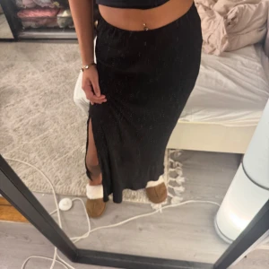 Svart långkjol med slits - Snygg svart långkjol med en subtil slits på sidan. Kjolen har en elegant och enkel design som passar perfekt för olika tillfällen. Den är gjord i ett bekvämt material som ger en fin passform.