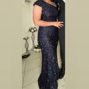 Festklänning - Elegant marinblå långklänning med glittrande paljetter. Klänningen har en smickrande passform och är ärmlös med en v-ringad design. Perfekt för festliga tillfällen. Kemtvätt. Har endast använts en gång!