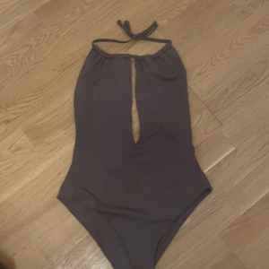 Brun baddräkt från Ann - Snygg brun baddräkt från Ann med halterneck-design och en stilren öppning framtill. Perfekt för en dag på stranden eller vid poolen. Baddräkten har en enkel och elegant stil som passar de flesta tillfällen. Aldrig använd. Prislapp kvar