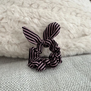 Lila och svart randigt scrunchie - Snyggt scrunchie med rosett i lila och svart randigt mönster. Perfekt för att ge en extra touch till din outfit.