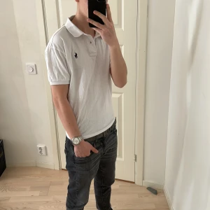 Ralph Lauren piké - Säljer en klassisk vit pikétröja från Polo Ralph Lauren med korta ärmar och broderad logga på bröstet. Perfekt för en stilren och avslappnad look. Tröjan har en traditionell krage och knappar framtill.