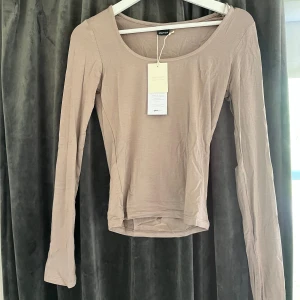 Beige långärmad topp från NA-KD - En stilren beige långärmad topp från Gina Tricot med rundad halsringning. Tillverkad i mjuk bomullsmix som ger en skön känsla. Perfekt att matcha med jeans eller kjol för en enkel och snygg look.