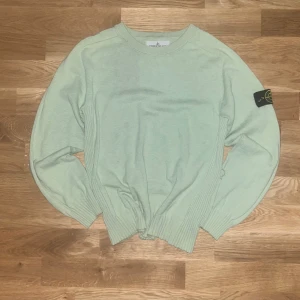 Ljusgrön stickad tröja från Stone Island Junior - Säljer en ljusgrön stickad tröja från Stone Island Junior med klassisk logotyp-patch på vänster ärm. Tröjan har rund halsringning och långa ärmar med ribbade muddar och sidor. Perfekt för dig som gillar stilrena plagg med exklusiv känsla. Passar bäst för barn från 153-160 cm