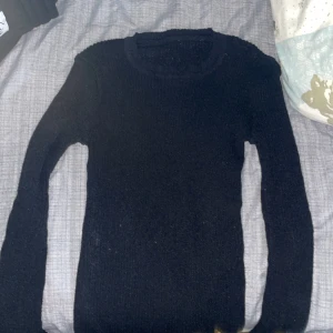 Svart stickad tröja med rund hals - En enkel och stilren svart stickad tröja med rund halsringning och långa ärmar. Perfekt att matcha med jeans eller kjol för en clean look. Mjuk och skön att ha på sig.