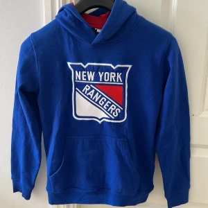 Blå New York Rangers hoodie NHL - Säljer en blå hoodie med New York Rangers-logga på bröstet. Tröjan har huva, magficka och långa ärmar. Perfekt för hockeyfans som vill visa sitt lagstöd. Officiell NHL-produkt.   Frågor eller funderingar är det bara att höra av sig!