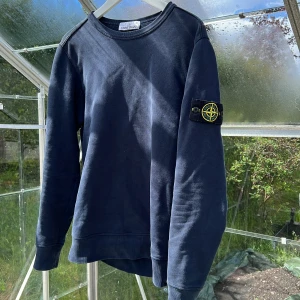 Mörkblå sweatshirt från Stone Island - Säljer en mörkblå stone Island tröja i storlek S men är lite liten i storleken.Tröjan har inga defekter och condition är 8/10. Tröjan har en stilren look och den ikoniska loggan på vänster arm. Köpt på NK för 2200, säljer pga för liten.