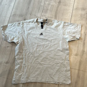 Beige t-shirt från Adidas - Säljer en stilren beige t-shirt från Adidas med liten broderad logga på bröstet. Klassisk passform och rund halsringning. Perfekt för en avslappnad look.