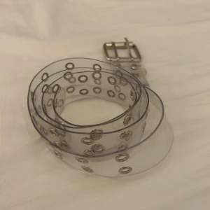 Transparent bälte med silverfärgade nitar - Säljer ett transparent bälte med dubbla rader av silverfärgade metallnitar och ett silverfärgat spänne. 
