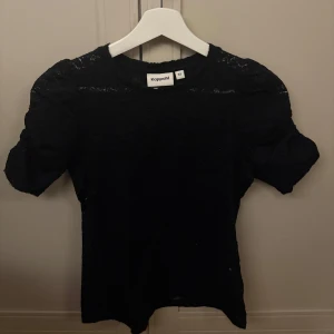 Svart spetsblus från Kappahl - Svart blus i spetsmaterial från Kappahl med korta ärmar och rund halsringning. Blusen har en elegant och feminin look med diskret mönstrad spets över hela plagget. Perfekt att styla med både jeans och kjol. 