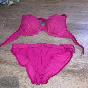Rosa bikini från Seekers - Snygg rosa bikini från Seekers med vadderad bygel-bh och matchande trosor. Överdelen har knyt i nacken och dekorativ spetsdetalj. Materialet är mjukt och stretchigt för en bekväm passform.