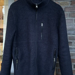 John henric  - Snygg mörkblå jacka i ull från John Henric med hög krage och tre dragkedjeförsedda fickor. Jackan har en stilren design och lång ärm, perfekt för kyligare dagar. Skick 9/10
