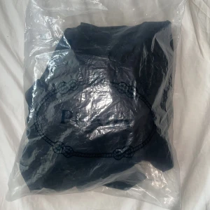 Svart hoodie från Prada - Säljer en svart hoodie från Prada med klassisk logga på bröstet och stor magficka framtill. Tröjan har huva med dragsko och är tillverkad i ett mjukt material. 