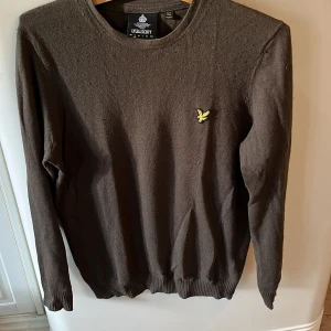 Mörkgrön tröja från Lyle & Scott - Mörkgrön tröja från Lyle & Scott med klassisk gul logga på bröstet. Tröjan har rund halsringning, långa ärmar och ribbade muddar vid ärmslut och nederkant. Inga tecken på slitningar eller fläckar förutom på lappen (se på sista bilden)