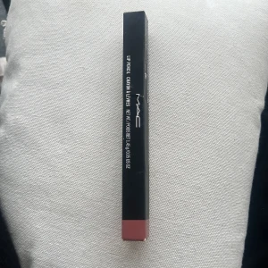 MAC Lip Pencil Boldly Bare - MAC Lip Pencil i nyansen Boldly Bare. En läppenna i en mjuk nude-rosa ton, perfekt för att definiera och forma läpparna. Kommer i klassisk svart MAC-förpackning med färgmarkering i botten.