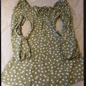 Grön klänning  - Säljer min gröna klänning med vita blommor. Aldrig använd utan bara provat den en gång. Saknar storlek men skulle säga att den är en M/L. Skriv för fler bilder. 