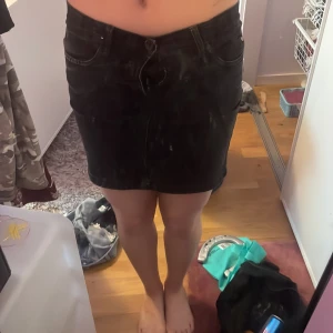 Svart jeanskjol med fickor - Säljer en svart jeanskjol med klassisk femficksdesign och knapp- samt dragkedjestängning framtill. Kjolen är kort och har en rak passform. Perfekt att styla med en enkel topp eller hoodie.