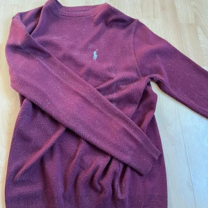 Vinröd tröja från Polo Ralph Lauren - Vinröd långärmad tröja från Polo Ralph Lauren med klassisk broderad logga på bröstet. Tröjan har rund halsringning och är tillverkad i ett mjukt material som passar perfekt till kyligare dagar.