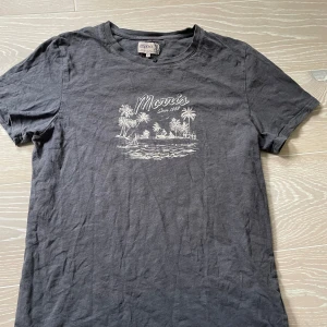 Mörkgrå t-shirt från Morris med tryck - Säljer en mörkgrå t-shirt från Morris i storlek M. T-shirten har ett vitt tryck framtill med palmer och texten 'Morris Since 1968'. Klassisk passform och rund halsringning. Perfekt för en avslappnad stil. Sitter perfekt på mig som är 180, t shirten kommer strykas innan frakt, hör av er för minsta lilla🤩🤝🏼