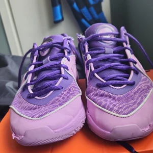 Kd 16 BAD - Säljer ett par lila Nike sneakers med snörning och rund tå. Skorna har en sportig design med mesh och syntetmaterial, samt tydliga Nike-loggor på sidan och baksidan. Snygga detaljer och bekväm passform, perfekta för träning eller vardag.