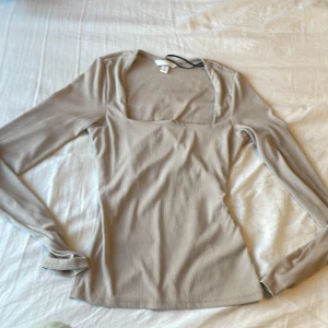 Beige ribbad topp med fyrkantig ringning! 💗 - Säljer en beige långärmad topp från H&M med ribbad struktur och snygg fyrkantig ringning. Toppen är figurnära och tillverkad i stretchigt material för en bekväm passform.💗 Säljs eftersom att den är för liten. Använd fåtal gånger🌺