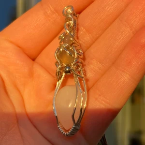 Handgjord silverberlock med silvertråd och vit sten - Unikt halsband med en vacker vit sten infattad i konstnärligt virad silvertråd. Hängsmycket har en elegant och organisk form, och kedjan är tunn och stilren. Perfekt för dig som gillar personliga smycken med boho-känsla.