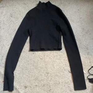 Svart croppad polotröja - Säljer en svart croppad polotröja med långa ärmar. Tröjan har en tight passform och är perfekt att styla med höga jeans eller kjol. Enkel och stilren design som passar till många olika outfits.