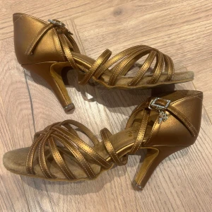 Shiny gold sandals with straps and open toe!🌟 - Selling a pair of shiny gold sandals with narrow straps and an open toe. The shoes have an elegant heel and buckle with rhinestone detail at the ankle. Perfect for standing out on the dance floor or for festive occasions.