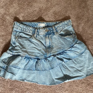Jeanskjol från Gina Tricot - Säljer en superfin jeanskjol från Gina Tricot i storlek 36/S Kjolen är i en härlig blå denim med volangdetaljer som ger en söt look. Perfekt för sommardagar eller en snygg våroutfit. Den har en klassisk jeansknapp och dragkedja framtill. Endast provad så den är som ny! Hör av er vid intresse!💕💕