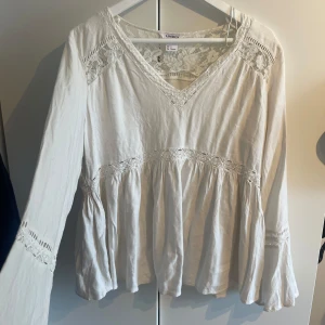 Bohemisk vit blus med spets från Lindex - Boho blus. Superfin vit blus från Lindex med v-ringning och spetsdetaljer vid axlar, ärmslut och midja. Blusen har långärmade, lite utsvängda ärmar och ett luftigt, flowy fall. Perfekt för dig som gillar  bohemisk stil.