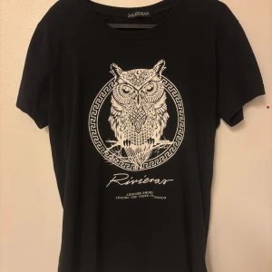 Svart t-shirt med uggletryck Jaleeman - Cool svart t-shirt från Jaleeman med ett stort vitt uggletryck och grafiska detaljer på bröstet. Klassisk rund halsringning och korta ärmar. Perfekt för dig som gillar unika prints och streetstyle.