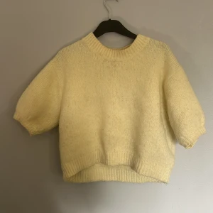 Gul stickad tröja från Zara - Supermysig ljusgul stickad tröja från Zara med korta ärmar och ribbad kant vid hals, ärmslut och nederkant. Tröjan har en loose passform och är lite croppad. Materialet är mjukt och fluffigt, vilket gör den extra skön att bära. Lite sminkfläckad vid kragen.