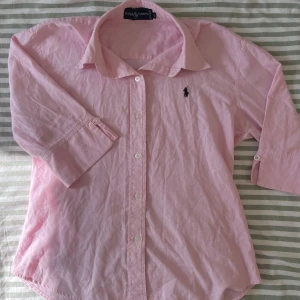 Rosa skjorta Ralph Lauren - Rosa skjorta från Ralph Lauren med broderad logga på bröstet. XL i barnstorlek, ungefär strl 164. Mycket fint skick.