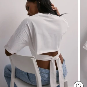 Vit croppad topp med knyt i ryggen - Säljer en vit croppad topp med korta ärmar och snygg knytning i ryggen. Toppen har en avslappnad passform och är perfekt att styla med höga jeans eller kjol. Enkel men trendig design som ger en cool look.
