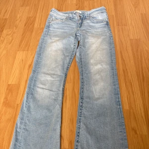 Ljusblå ginatricot bootcut jeans med slitningar - Säljer ett par ljusblå bootcut jeans med klassisk femficksdesign och snygga slitningar vid bensluten. Jeansen har låg midja och är tillverkade i mjukt denimtyg. Perfekta för en avslappnad och trendig look. Bra skick, lite skada där nere på byxornas kant bara
