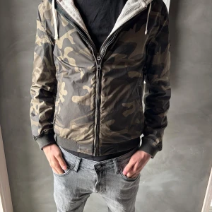 Woolrich jacka - Säljer en snygg jacka från Woolrich med klassiskt camouflage-mönster i gröna och beige toner, Jackan går även att vända ut och in till en mörkare färg. En eftertraktad färg och är den perfekta jackan till sommarn.