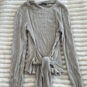 Beige ribbad omlottopp från Zara - Superfin beige ribbad topp från Zara med omlottdetalj och knyt framtill. Långärmad och i mjukt, stretchigt material. Knappt använd. Går att använda bak och fram, samt knyta på olika sätt. 
