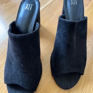 Svarta mocka mules från XIT - Svarta mules från XIT i mjuk mocka med öppen tå och bred klack. Skorna har en stilren och minimalistisk design med platt sula framtill och bekväm passform. Använt 1 gång. Köpta för 500kr, säljer för 200kr. Pris kan diskuteras.