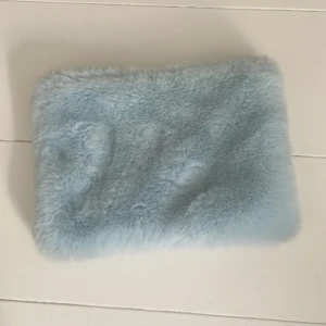 Ljusblå fluffig necessär  - Supermjuk och fluffig ljusblå necessär eller pennskrin i fuskpäls med dragkedja upptill. Perfekt att ha till smink eller småprylar. Tyvärr saknas en del av dragkedjan men den fungerar fortfarande och det finns en liten mörkare blå missfärgning på ena sidan men den är inte jätte synlig. Necessären är ganska liten. 