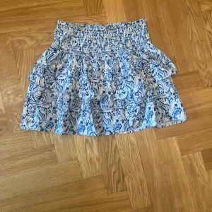 Blåvit volangkjol från Gina Tricot - Supersöt kort volangkjol från Gina Tricot i blått och vitt mönster. Kjolen har smock i midjan och flera lager volanger. Storlek 158/164 men passar mig perfekt som oftast har kläder i S!