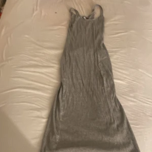 Grå långklänning med smala axelband - Enkel och stilren grå långklänning med smala axelband. Klänningen har en rak passform och är ärmlös, perfekt för en avslappnad och cool look. Materialet känns mjukt och följsamt mot kroppen.