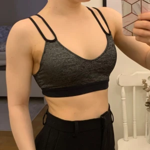 Svart sportig linnetopp från Nike - Sportopp från Nike med dubbla tunna axelband. Silver/svart/grå i färgen. Löstagbar vaddering.