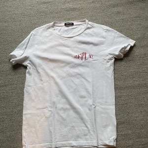 Vit Replay t-shirt med tryck - Vit t-shirt från Replay med röd logga på bröstet, detaljerat svart tryck på ryggen. Tröjan är endast använd 2 gånger. Nypris 1000kr