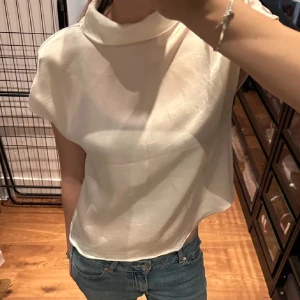 Vit sidenblus från Zara - Säljer denna superfina vita blusen i siden med korta ärmar och hög krage. Från Zara! Blusen har en snygg knäppning med små knappar i ryggen🥰